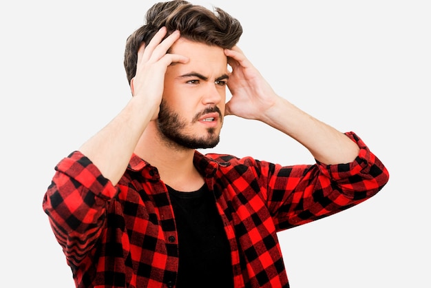 Avoir quelques ennuis. Jeune homme frustré tenant la tête dans les mains et regardant loin en se tenant debout sur fond blanc