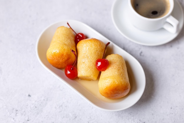 Baba au rhum napolitain ou baba au rhum sur une assiette blanche avec une cerise à cocktail et une tasse de café