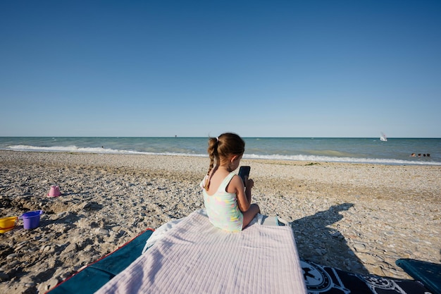 Baby Girl sitting and play phone at sea beach Porto Sant Elpidio Italie