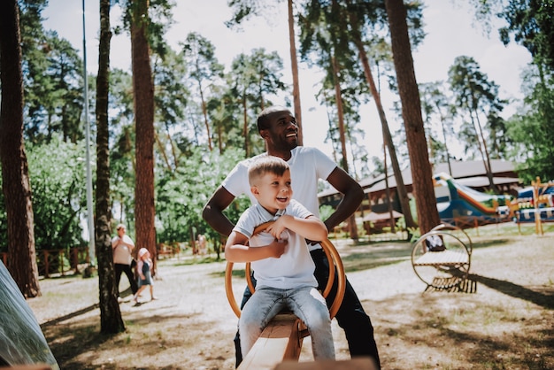 Photo babysitter mâle et enfant sur le terrain de jeu jouent à la bascule.