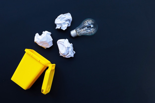 Bac jaune avec ampoule et papier froissé blanc sur mur sombre. Idées et concept de pensée créative. Vue de dessus