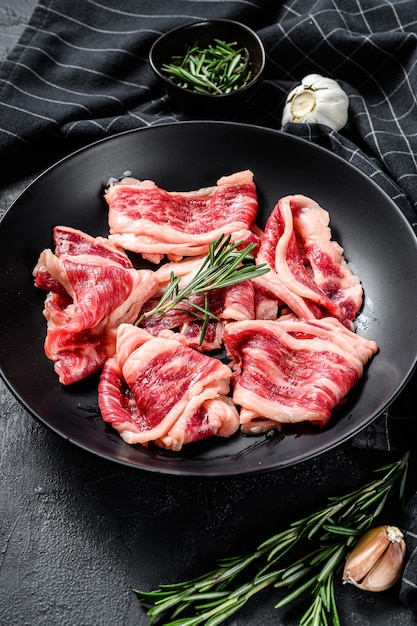 Bacon de boeuf cru, viande marbrée dans une assiette. Fond noir. Vue de dessus.