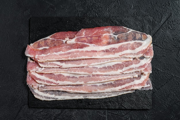 Photo bacon cru sur une planche à découper en pierre. la viande de porc. fond noir. vue de dessus