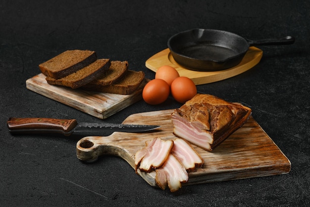 Bacon de porc fumé avec du pain brun et des œufs sur une planche à découper en bois