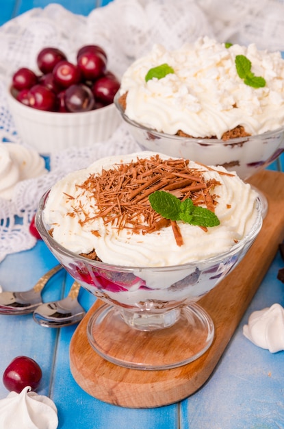 Bagatelle anglaise avec biscuit au chocolat, crème fouettée, cerise et meringue dans un verre sur bois