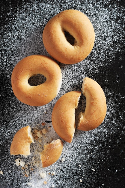 Des bagels frais et savoureux, entiers et cassés sur un fond métallique noir.