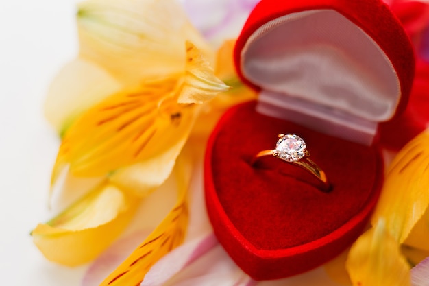 Photo bague diamant de fiançailles dans une boîte cadeau rouge sur un tas de pétales de fleurs. symbole de l'amour et du mariage.