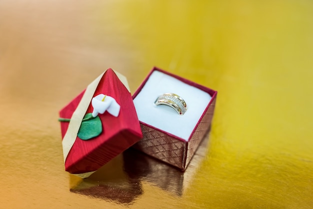 Bague dorée dans une boîte cadeau rouge sur fond doré