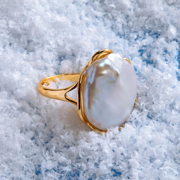 Bague dorée perle baroque élégante de luxe sur fond de neige blanche. Photo en gros plan