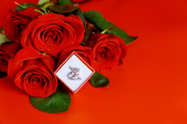 Bague de fiançailles et belle rose rouge sur fond rouge. La Saint-Valentin.