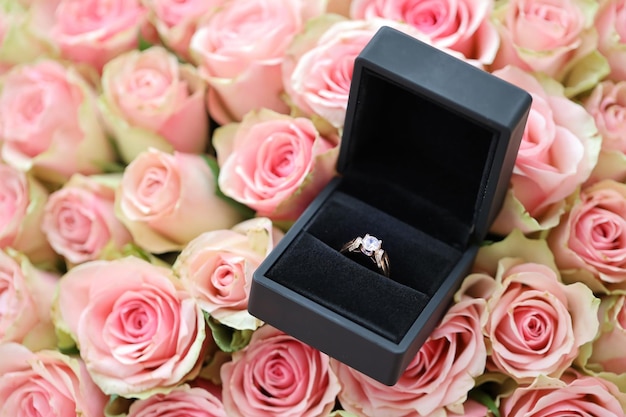 Une bague de fiançailles en diamant d'or dans une boîte noire parmi une grande quantité de roses dans un grand bouquet en gros plan
