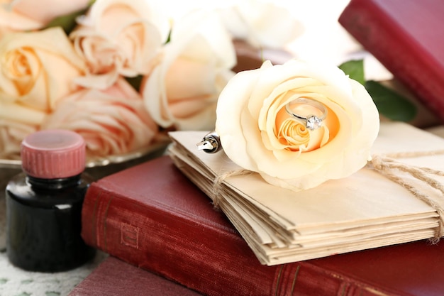 Bague de mariage en fleur rose fraîche avec vieux livre et lettres sur fond de table en bois de couleur. Notion de cru