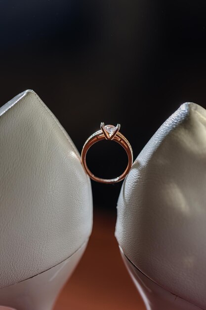 Bague en or de la mariée avec un galet entre des chaussures blanches à talons Bague précieuse de la mariée