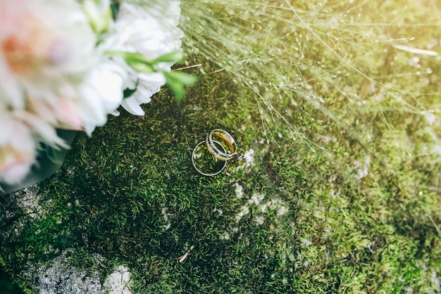 Des bagues de mariage posées sur la mousse à l'extérieur Un bouquet de fleurs est à proximité Détails de bijoux de fiançailles