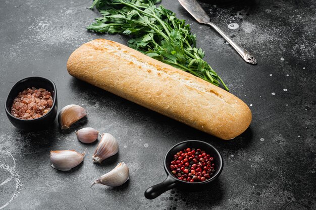 Baguette de pain grillé avec ensemble d'ingrédients à l'ail et aux herbes, sur fond de table en pierre noire foncée