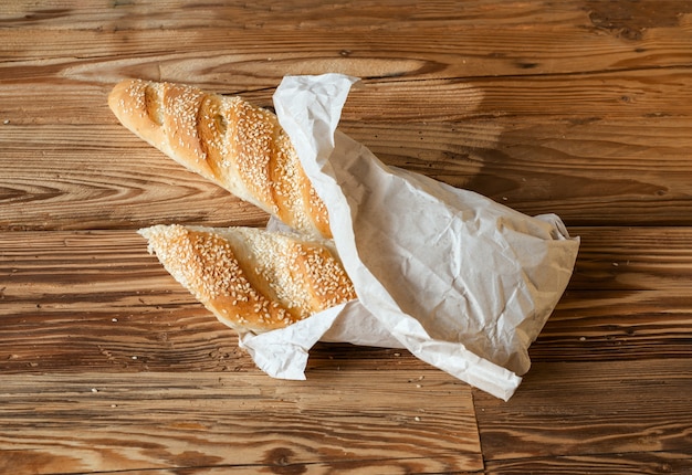 Baguette de pain sésame saupoudré de sésame avec du papier d'emballage sur une table en bois