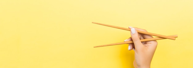 Baguettes en bois tenues avec des mains féminines sur fond jaune. Prêt à manger des concepts avec un espace vide.