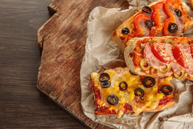 Baguettes de pizza chaudes aux olives paprika salami et jambon sur table en bois