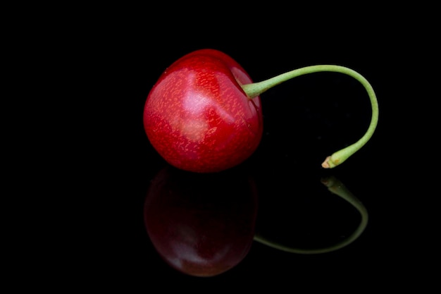 Photo une baie de cerise et une petite tige verte sur fond noir avec un reflet.