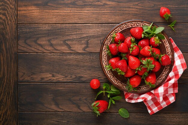 Baie de fraise Fraise rouge fraîche dans une assiette rustique en céramique dans un panier sur une table rustique en bois agrandi Délicieuses baies rouges juteuses Vue de dessus avec espace de copie