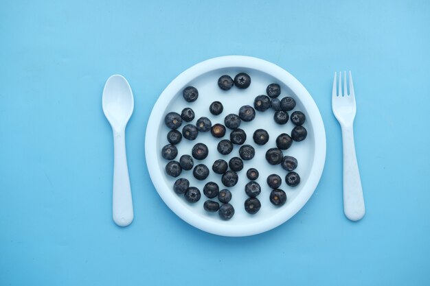 Baies bleues fraîches sur une assiette sur fond bleu