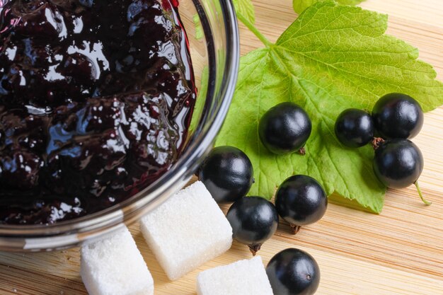 Baies de cassis mûres sur la table de la cuisine à côté d'un bol de confiture de groseilles et de morceaux de sucre macrophotographie en gros plan