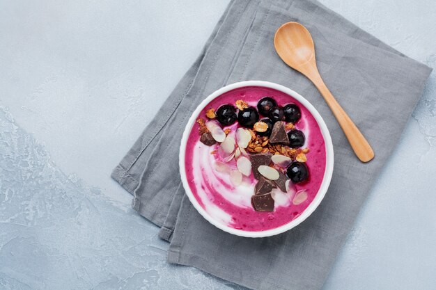 Baies de cassis rose, bol de smoothie à la banane avec granola, flocons d'amandes et chocolat sur fond de béton gris clair