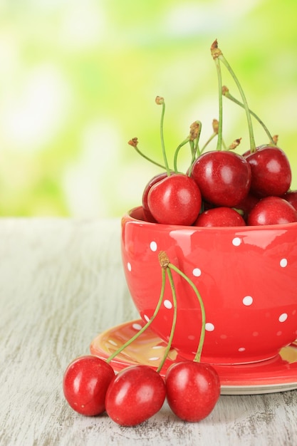 Baies de cerise dans une tasse sur une table en bois sur fond clair