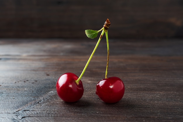 Baies de cerises fraîches mûres sur une branche avec une feuille sur un fond rustique en bois.