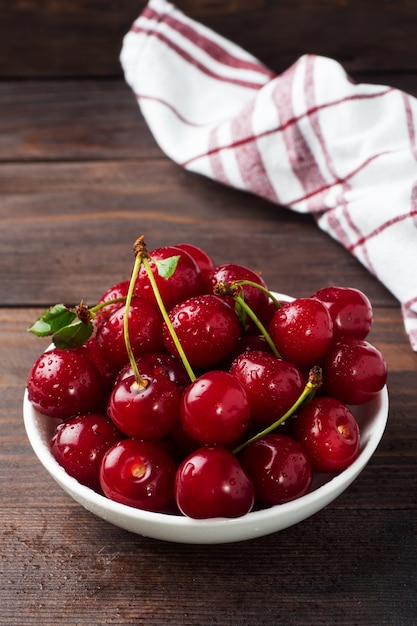 Baies de cerises fraîches mûres dans une assiette, fond en bois rustique foncé. Espace de copie.