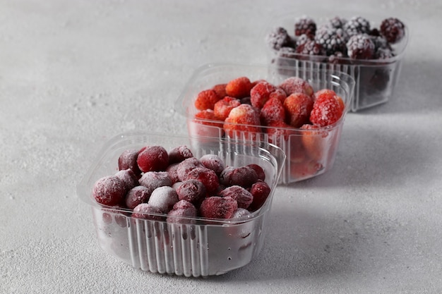 Baies congelées telles que cerises, fraises et mûres dans les boîtes de rangement sur fond gris clair.