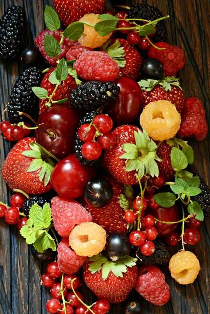 Baies d'été sur un gros plan de planche de bois. Petits fruits comme les fraises, les bleuets, les groseilles rouges, les framboises et les mûres sur une planche de bois.