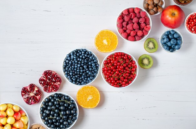 Baies fraîches, fruits, noix sur un fond en bois blanc.