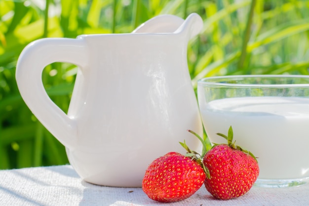 Baies de fraise, une cruche et une tasse de lait sur une serviette sur fond d'herbe