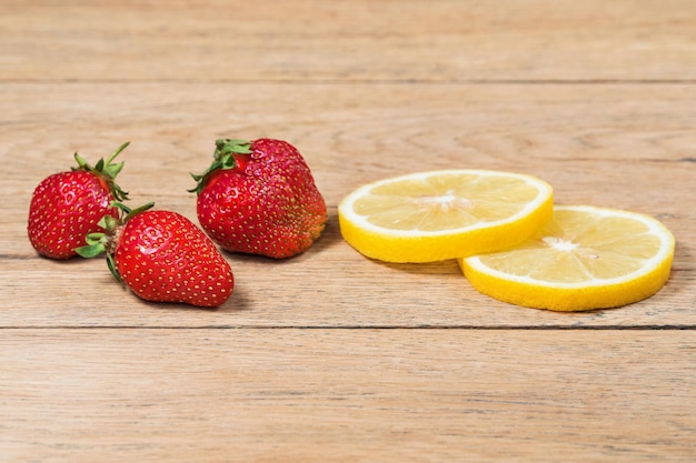 Baies de fraises mûres et deux tranches de citron sur une vieille table en bois