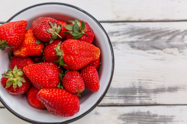 Baies de fraises rouges mûres dans un bol sur un fond en bois clair. Vitamines saisonnières. Fermer. Vue de dessus.