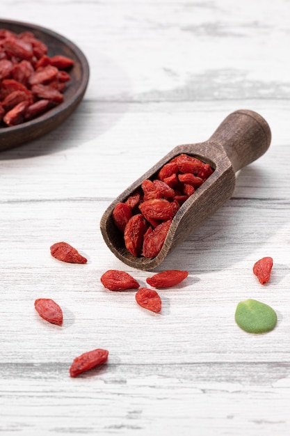 Des baies de goji séchées avec une cuillère en bois sur une plaque en bois sur fond blanc Format vertical