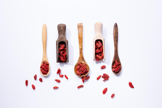 Photo des baies de goji séchées sur des cuillères en bois isolées sur un fond blanc