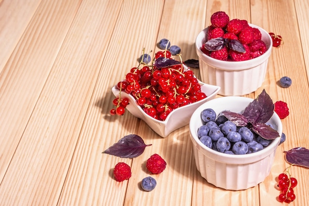 Baies mûres assorties dans des bols. Framboises fraîches, myrtilles et groseilles rouges. Table de planches en bois, espace de copie