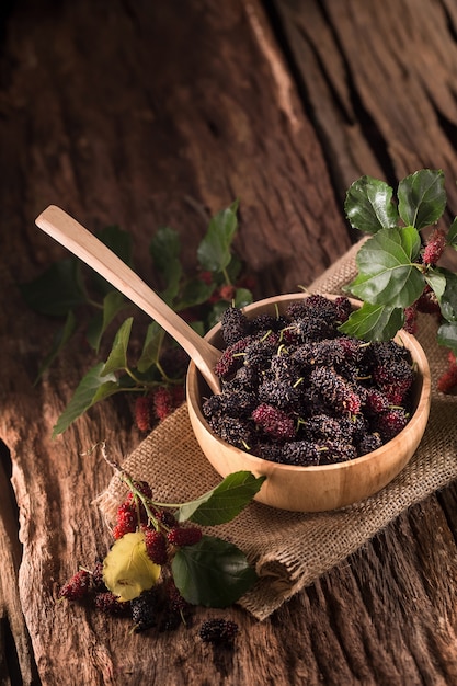 Baies de mûrier dans une tasse en bois sur un fond en bois