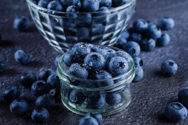 Baies naturelles biologiques de bleuets avec des gouttes d'eau sur fond sombre gros plan de bleuets dans une assiette en verre