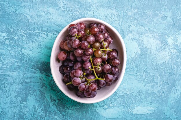 Les baies de raisin mûres fraîches dans un bol sur bleu texturé