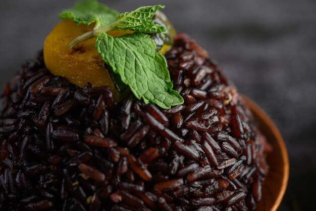 Des baies de riz violet cuites dans un plat en bois avec des feuilles de menthe et de citrouille