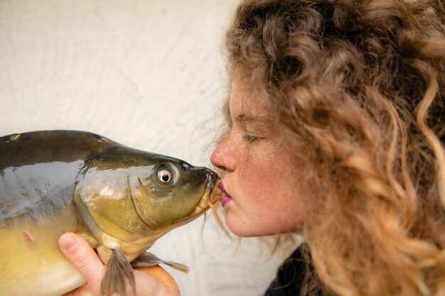 Photo le baiser - une jeune femme belle aux cheveux bouclés embrasse une carpe