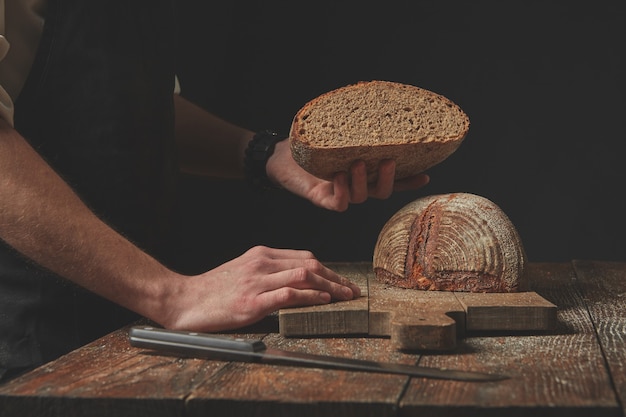 Baker conserve la moitié du pain biologique fraîchement cuit sur un fond sombre