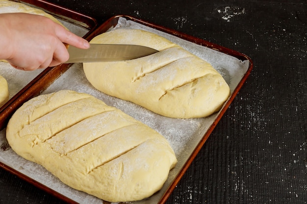 Baker coupe la pâte à pain non cuite maison sur une grille prête pour la cuisson.