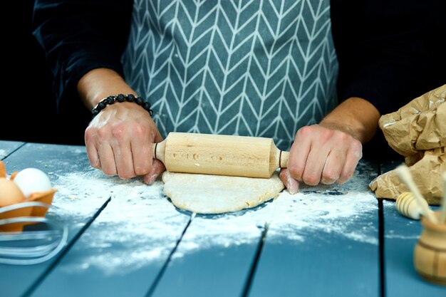 Baker mains préparant la pâte fraîche avec rouleau à pâtisserie sur la table de la cuisine. Homme formant la pâte sur une surface farinée.