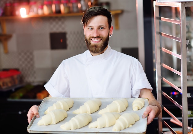 Baker met au four les croissants crus de la boulangerie