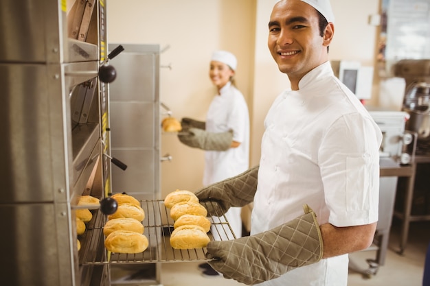 Photo baker souriant à la caméra prenant des rouleaux de four