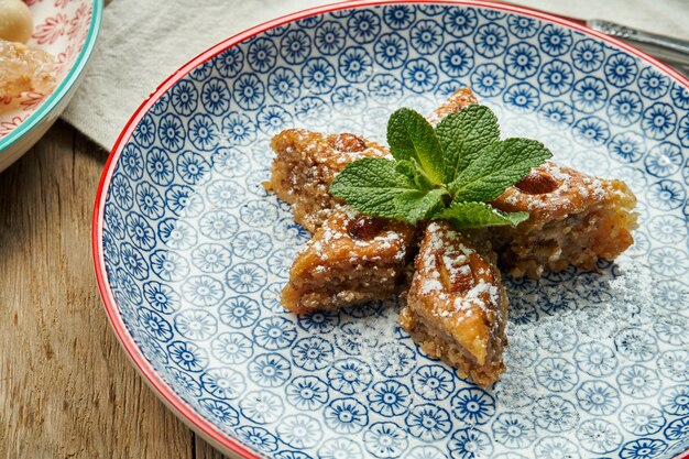 Baklava turc classique avec pistaches et miel dans une plaque en céramique sur une surface en bois. Pâtisseries et bonbons turcs. Fermer